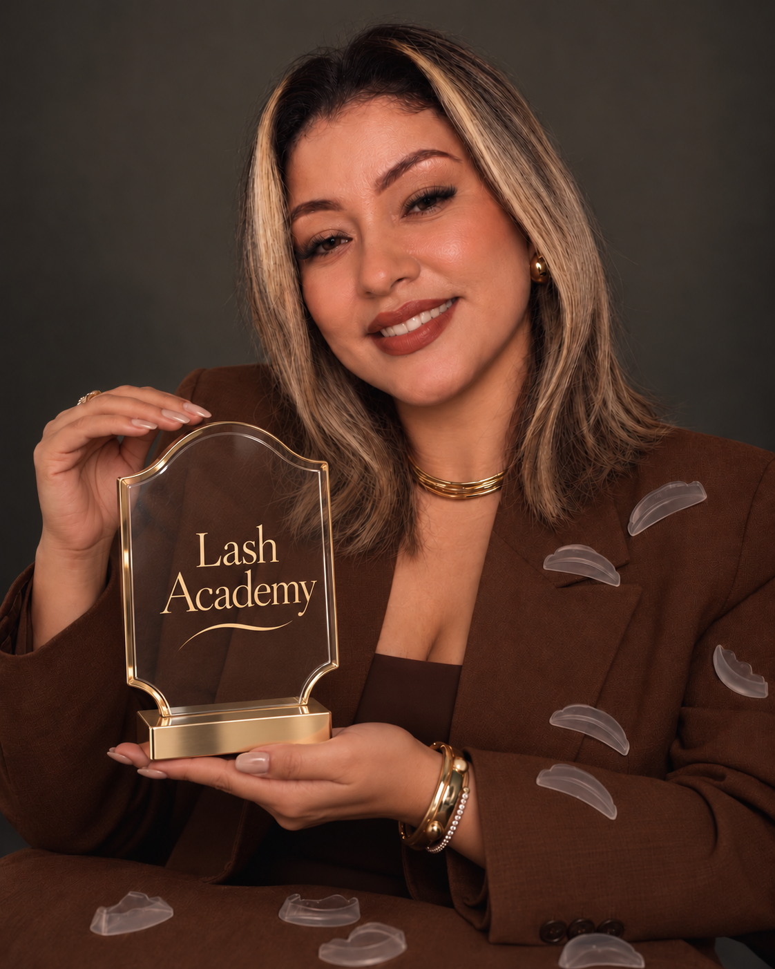 Bianca Dias sorrindo, de blazer marrom, segurando uma pequena placa de troféu com o nome Lash Academy.